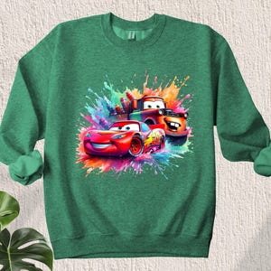 May include: Green sweatshirt with a colorful graphic of two cartoon cars, one red and one orange, with paint splatters in the background.