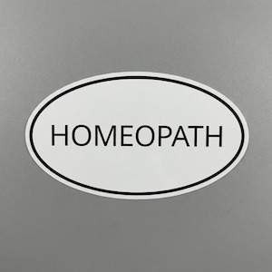 May include: White oval sticker with a black border and the word "HOMEOPATH" in black, centered. The sticker is on a gray surface.