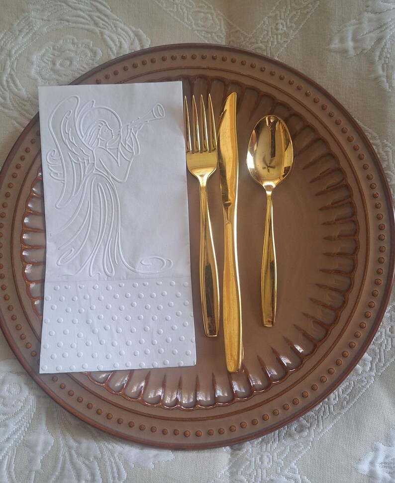 Pu&ograve; includere: Un set di forchetta, coltello e cucchiaio dorati su un piatto marrone con bordo decorativo. Un tovagliolo bianco con un disegno a rilievo di un angelo &egrave; posto sul piatto. Le posate sono disposte per una cena formale.