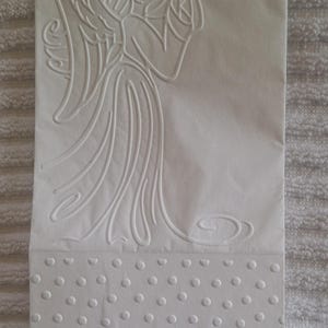 Pu&ograve; includere: Carta bianca goffrata con un angelo che suona la tromba. L'angelo ha grandi ali e un'aureola. La parte inferiore della carta presenta un motivo a pois. La carta rettangolare &egrave; probabilmente per un biglietto di auguri o un invito.