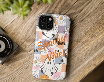 Könnte beinhalten: Eine weiße iPhone-Hülle mit einem bunten Muster aus Geistern, Blumen und karierten Quadraten. Der Text "Spooky Vibes" ist in Orange auf der Hülle gedruckt.