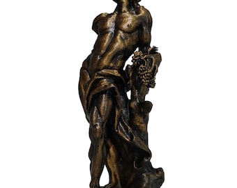 May include: A bronze-colored sculpture of a standing figure with a muscular build, draped in fabric around the waist. The figure leans against a tree trunk adorned with a cluster of grapes, with the head tilted upward and eyes looking toward the sky.
