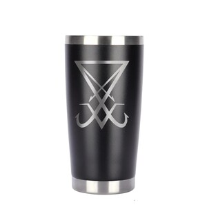 May include: Black stainless steel tumbler with a silver rim and base. The tumbler features a silver graphic of a sigil. The design is centered on the tumbler. The tumbler is cylindrical and appears to be insulated.