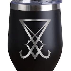 May include: Black stemless wine tumbler with a silver-colored sigil design. The tumbler has a clear lid and a stainless steel rim. The sigil is a stylized symbol with a triangle and inverted hooks.