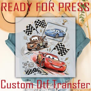 May include: A light gray graphic featuring cartoon cars, checkered flags, and the text "READY FOR PRESS" and "Custom Dtf Transfer". The design includes a red race car, a brown tow truck, and a blue sports car.