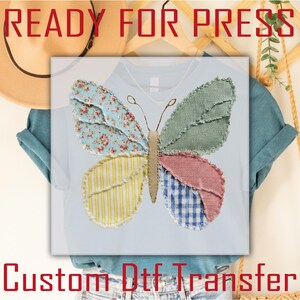 May include: A light blue t-shirt featuring a colorful butterfly design. The butterfly is made of various fabrics, including floral, striped, and gingham patterns. The text "READY FOR PRESS" is at the top, and "Custom Dtf Transfer" is at the bottom.