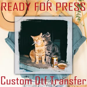 May include: A square image with a distressed border features two cats. One orange tabby cat has a cigarette in its mouth, while a gray tabby cat nuzzles it. A beer can and a small bowl are visible. Text at the top reads "READY FOR PRESS" and at the bottom "CUSTOM DTF TRANSFER".