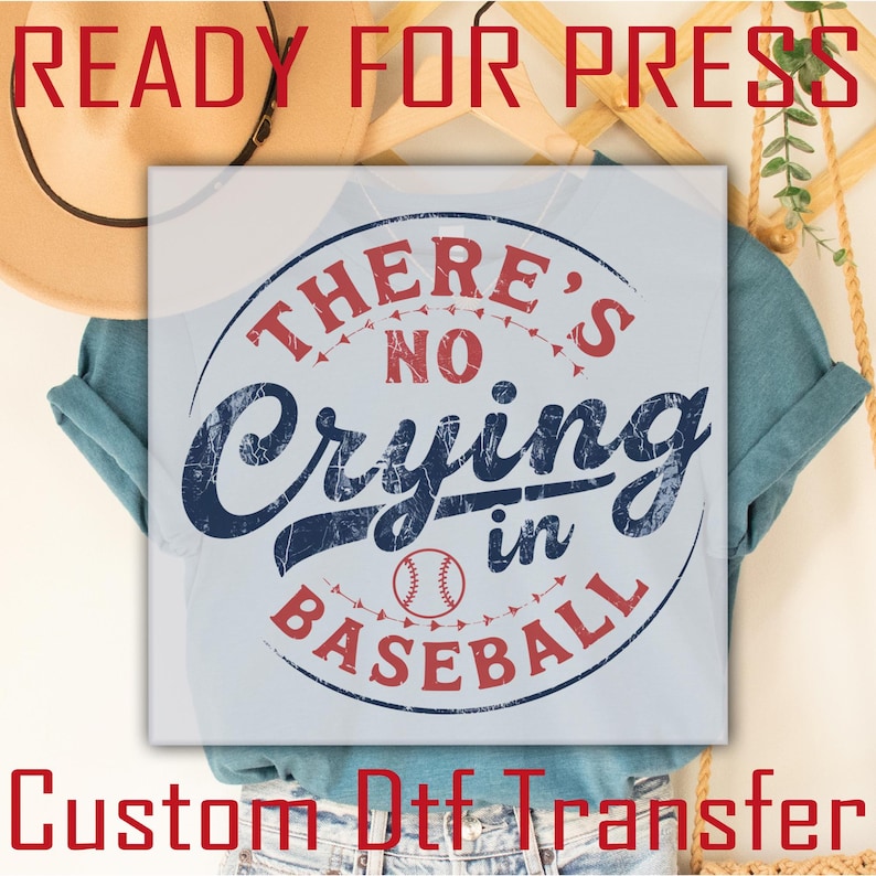 A light blue t-shirt with a distressed, vintage-style graphic that reads "There's No Crying in Baseball" with a red baseball graphic in the center. The graphic is surrounded by a red circle with white stitching.
