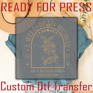 May include: A gray t-shirt with a gold design that reads "A Well-Read Woman is a Dangerous Creature". The design features a book, flowers, and moons.