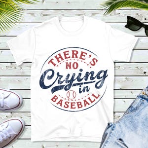 White t-shirt with a red and blue distressed circle graphic that says "There's No Crying in Baseball" with a baseball graphic inside the circle.