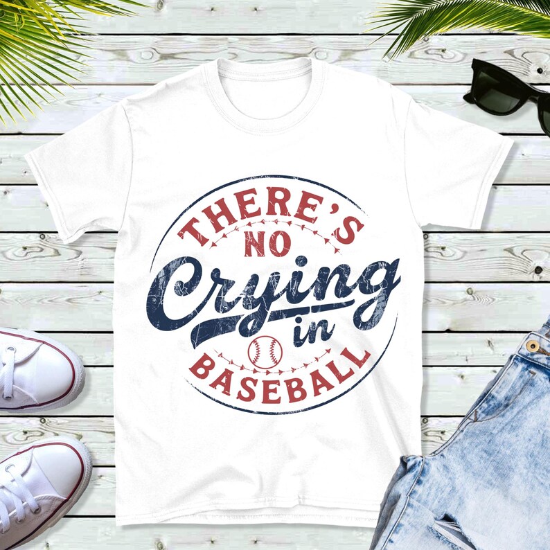 White t-shirt with a red and blue distressed circle graphic that says "There's No Crying in Baseball" with a baseball graphic inside the circle.