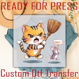 May include: A light blue t-shirt featuring a cartoon cat with an angry expression holding a broom, chasing a mouse holding a "CHILL!" sign. The text "READY FOR PRESS" and "Custom Dtf Transfer" are at the top and bottom.