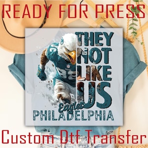 May include: A white t-shirt with a green and white image of a football player with the text "They Not Like Us Eagles Philadelphia" on it. The image is a digital design for a custom iron-on transfer.