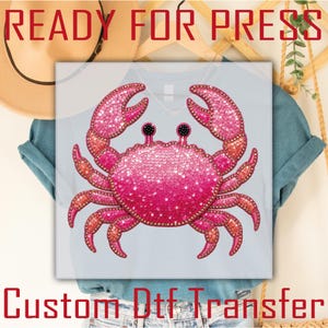 May include: A pink sequined crab design on a light blue t-shirt. The crab has a gradient effect, transitioning from a darker pink to a lighter shade. The text "READY FOR PRESS" and "Custom Dtf Transfer" are visible.