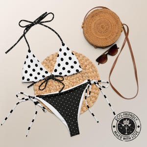 May include: Black and white polka dot bikini with a halter top and a high-cut bottom. The bikini is on a woven straw mat with a brown wicker bag and sunglasses.