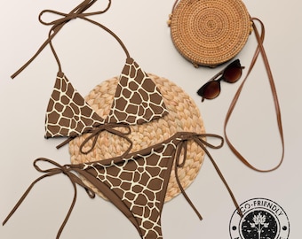 May include: A two-piece bikini set featuring a brown and white giraffe print pattern with tie-side bottoms and a triangle top. Included are a round woven straw crossbody bag with a long strap and dark brown sunglasses with tinted lenses.