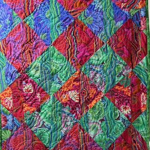 May include: A quilt featuring a repeating diamond pattern composed of vibrant fabric squares. The design incorporates floral motifs, wavy lines, and abstract shapes in saturated shades of magenta, purple, orange, and green, with visible machine quilting stitches throughout.