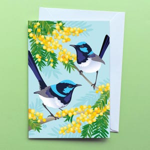 May include: Two blue and black birds with bright blue heads perched on branches of a tree with yellow flowers. The background is a light blue.