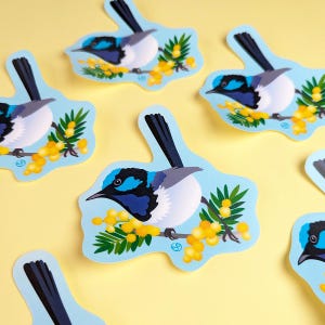 Könnte beinhalten: Ein Set mit sechs bunten Aufklebern, die einen blauen, schwarzen und weißen Vogel zeigen, der auf einem Zweig mit gelben Blüten sitzt. Die Aufkleber befinden sich auf einem hellgelben Hintergrund.