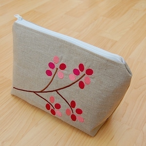 Puede incluir: Una bolsa de cremallera de lino gris con un diseño floral bordado en rosa y rojo.