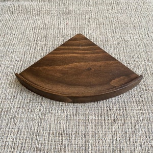 May include: A dark brown wooden corner shelf with a rounded edge. The shelf is made of solid wood and has a natural finish.