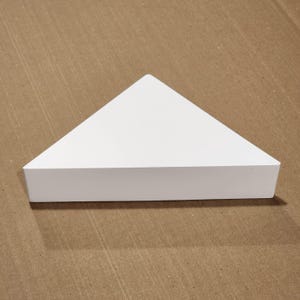 May include: White triangular shelf made of wood. The shelf is a geometric shape with a flat top and three sides.