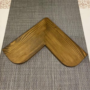 May include: A wooden corner shelf with a warm brown stain. The shelf is V-shaped, with rounded corners, and displays the natural wood grain. This shelf is designed to fit into a corner, maximizing space.