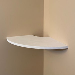 Puede incluir: Una estanter&iacute;a de esquina blanca con un borde frontal curvo. La estanter&iacute;a triangular es de madera y est&aacute; montada en una pared beige. Ofrece una soluci&oacute;n de almacenamiento que ahorra espacio para una esquina de la habitaci&oacute;n. Medidas: aprox. 30 cm.