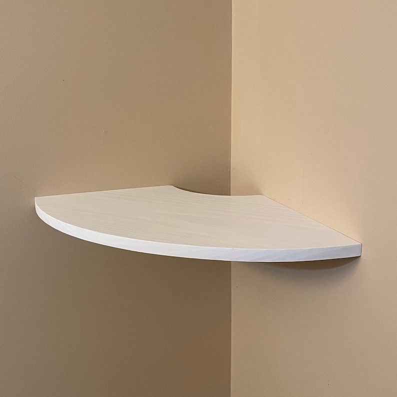 Puede incluir: Una estanter&iacute;a de esquina blanca con un borde frontal curvo. La estanter&iacute;a triangular es de madera y est&aacute; montada en una pared beige. Ofrece una soluci&oacute;n de almacenamiento que ahorra espacio para una esquina de la habitaci&oacute;n. Medidas: aprox. 30 cm.