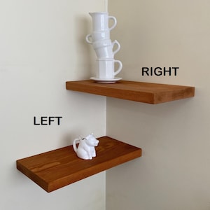 May include: Two wooden shelves mounted on a wall in a corner. The top shelf has a stack of white ceramic cups and a saucer. The bottom shelf has a white ceramic pig figurine. The shelves are labeled "LEFT" and "RIGHT".