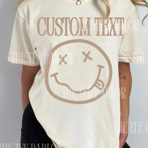 May include: A white t-shirt with a brown smiley face graphic and the text "CUSTOM TEXT" printed on the front.