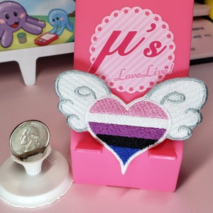 May include: A heart-shaped embroidered patch with a genderqueer pride flag design. The patch has white wings and is attached to a pink background with the text "μ's Love Live!"