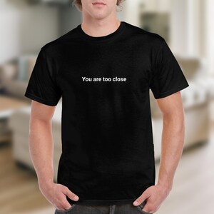 Może przedstawiać: Czarny T-shirt z nadrukiem "You are too close" w kolorze białym na przodzie.
