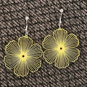 May include: A pair of yellow flower-shaped earrings. Each earring features a delicate, openwork design with radiating lines, creating a floral pattern. The earrings have silver-colored ear wires for easy wear. The earrings are a bright, cheerful accessory.