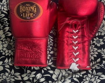May include: A pair of red boxing gloves with white laces. The gloves have a gold logo that says "No Boxing No Life" and "Hecho en Mexico".
