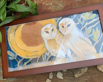 May include: A framed watercolour painting depicting two owls with white and tan plumage. The artwork includes a yellow moon and blue foliage, set against a dark background. The frame is a dark brown colour.