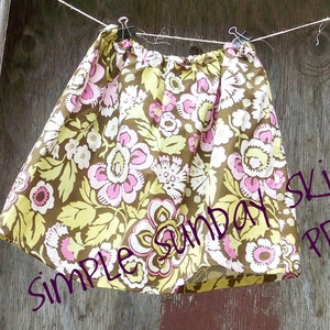 May include: A brown and yellow floral skirt with a white elastic waistband. The skirt is hanging on a clothesline and the text "Simple Sunday Skirt PDF" is written in purple on the right side of the image.