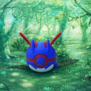 May include: A blue and red spherical figure with red antennae, set against a lush green forest backdrop. The figure has a white base and red accents. The forest scene features green foliage and trees, creating a vibrant, natural setting.