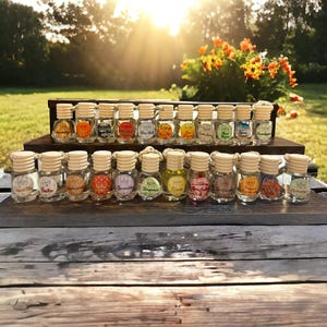 May include: A collection of 24 small glass bottles with colorful labels and wooden caps. The bottles are arranged on a wooden shelf with a natural wood grain. The bottles are filled with a clear liquid and have a string attached to the cap. The bottles are labeled with different scents, such as "Vanilla", "Cake", "Lavender", "Bergamot", "Citrus", "Strawberry", "Orange", and "Cinnamon".