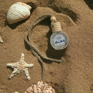 May include: A small, round, clear glass bottle with a wooden cap and a hanging cord, featuring a label that reads Sea Salt. The bottle is accompanied by a white seashell, a starfish, and a cluster of small, light-coloured coral fragments.