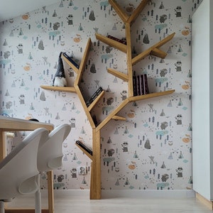 May include: A wooden tree-shaped bookshelf with multiple shelves, featuring a whimsical woodland animal print wallpaper. The bookshelf is filled with books and a small gnome figurine. Two white chairs are in the foreground.