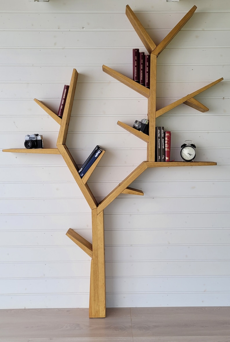 May include: A wooden bookshelf shaped like a tree with multiple branches and shelves. The shelves are filled with books, a camera, and an alarm clock.