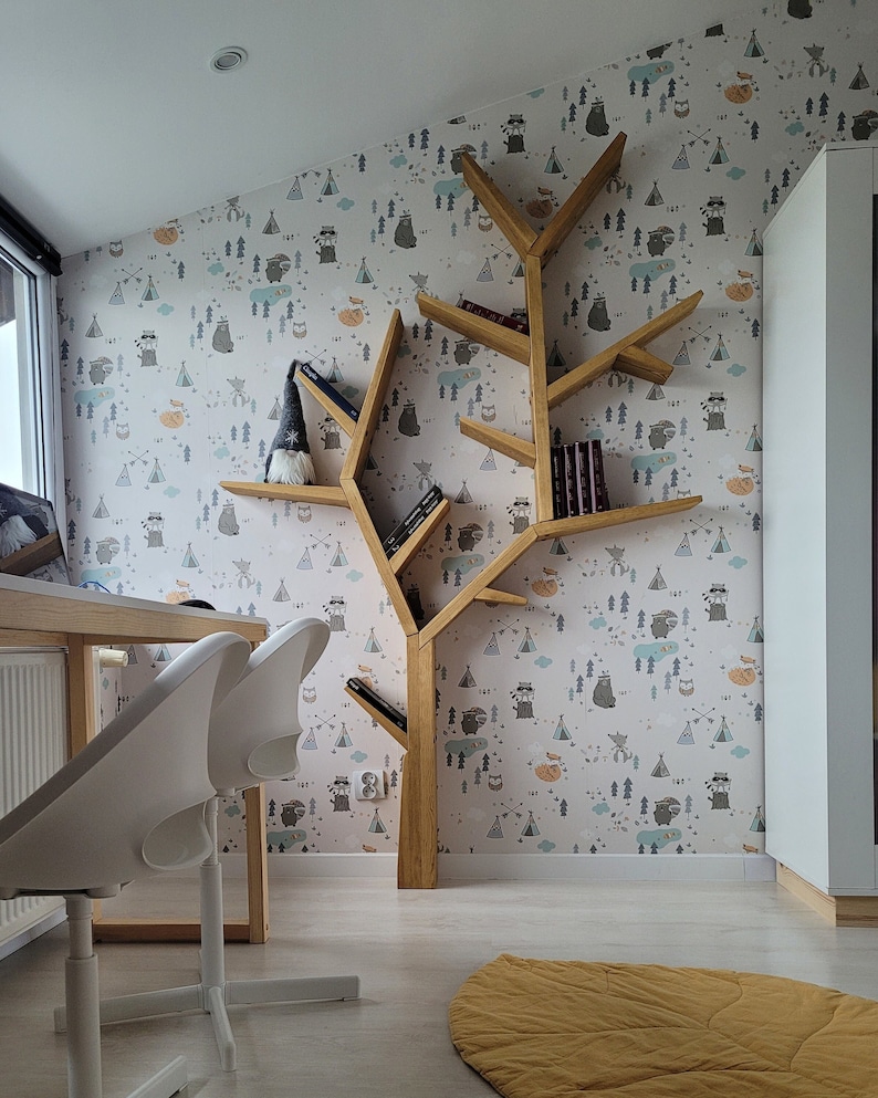 May include: A wooden tree-shaped bookshelf with multiple shelves, featuring a whimsical woodland animal print wallpaper. The bookshelf is filled with books and a small gnome figurine. Two white chairs are in the foreground.
