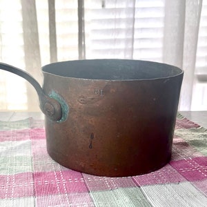 May include: A vintage copper saucepan with a black handle. The saucepan has a green patina and is marked with the number "11".
