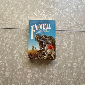May include: A paperback book titled "Footfall" by Larry Niven and Jerry Pournelle. The cover features a colorful illustration of a large, gray, elephant-like creature with a red bag on its back. The creature is standing on a pile of debris in a field.