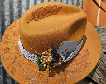 May include: A brown felt fedora hat with a floral design and a leaf embroidered on the crown. A playing card with the word "JOKER" is tucked into the hat band.