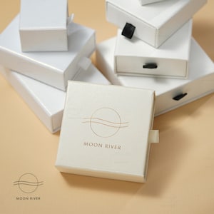 May include: White gift boxes with a gold logo of a circle with a wavy line inside and the text "MOON RIVER".