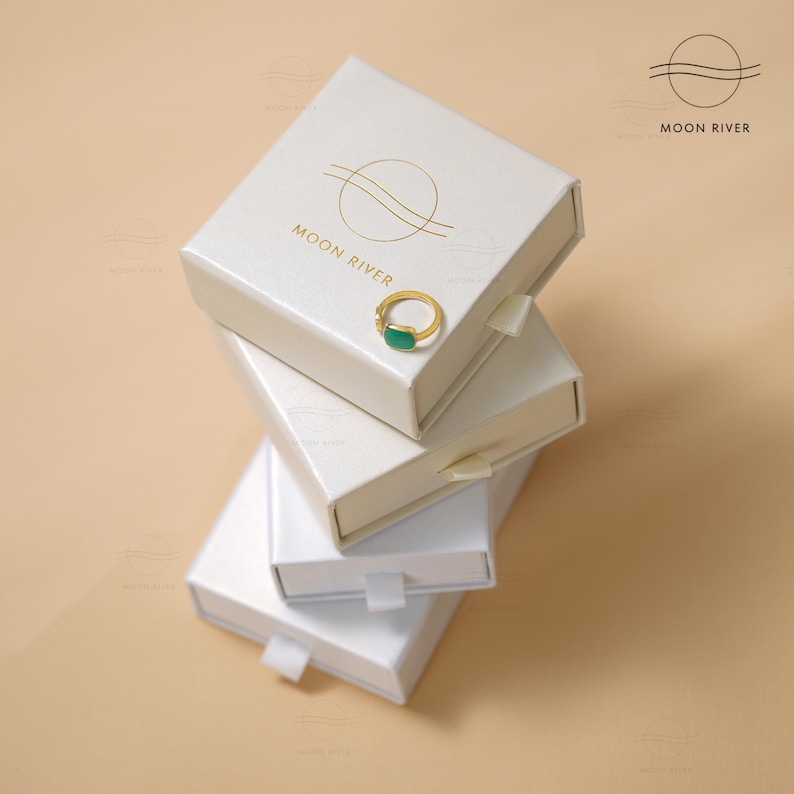 May include: A stack of four white boxes with a gold logo that says "Moon River". The top box has a green ring inside.