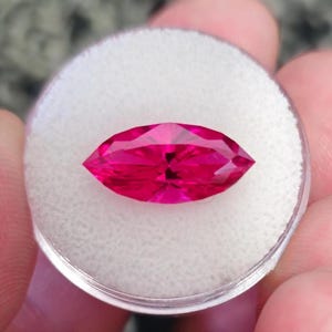 May include: A vibrant pink marquise-shaped gemstone displayed on a white background.