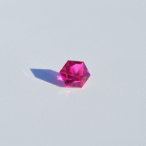 May include: A bright pink gemstone with a hexagonal shape, cut into a faceted design.